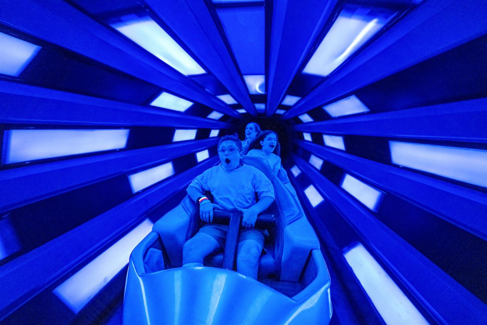 Visitantes a bordo de um foguete da Space Mountain, dentro do túnel iluminado de azul da atração